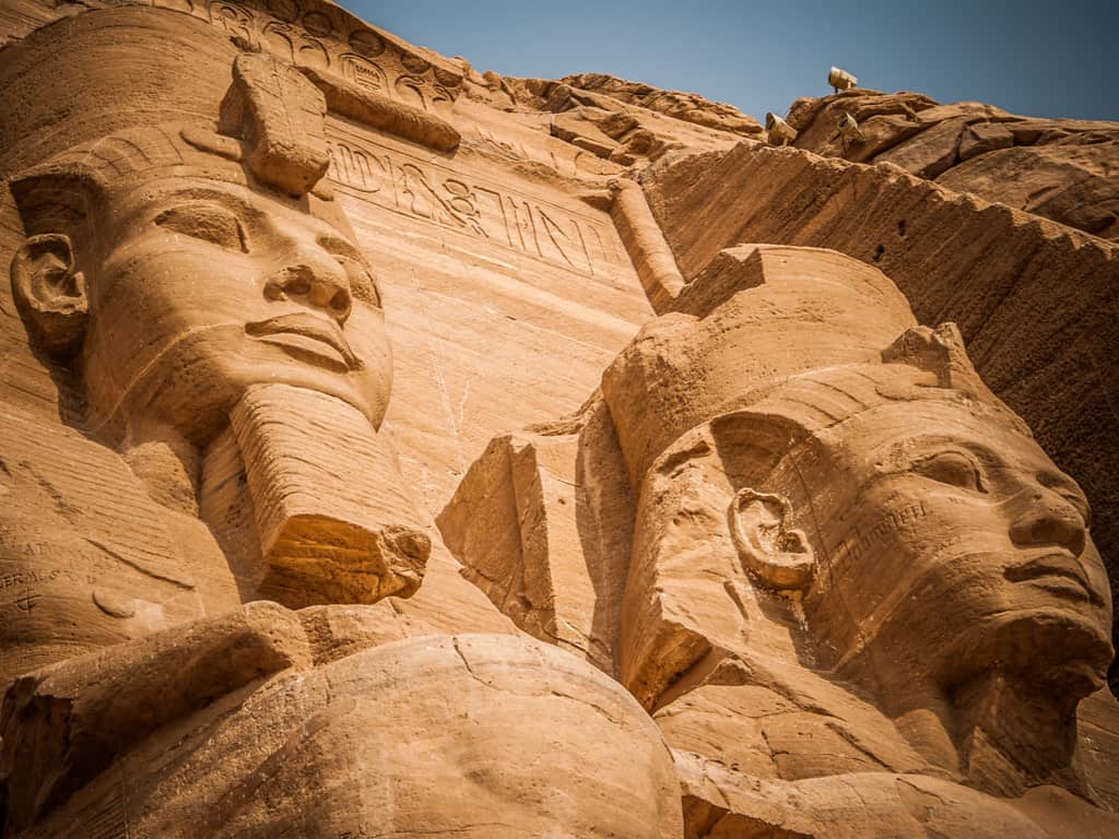"The grand facade of Abu Simbel temples, with colossal statues of Pharaoh Ramses II, against a clear blue sky.