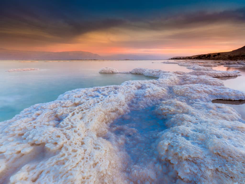 A tranquil sunrise over the Dead Sea, with salt deposits creating a unique landscape.