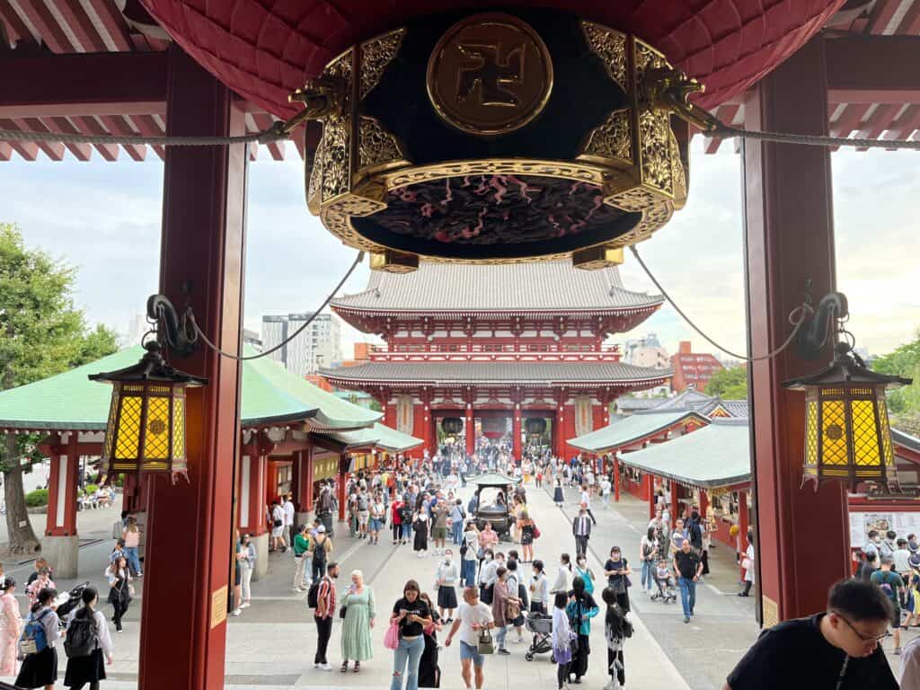 View from Senso-ji Temple's Main Hall towards the Hozomon Gate, showcasing the bustling Nakamise Street lined with visitors and shops in Tokyo, Japan.