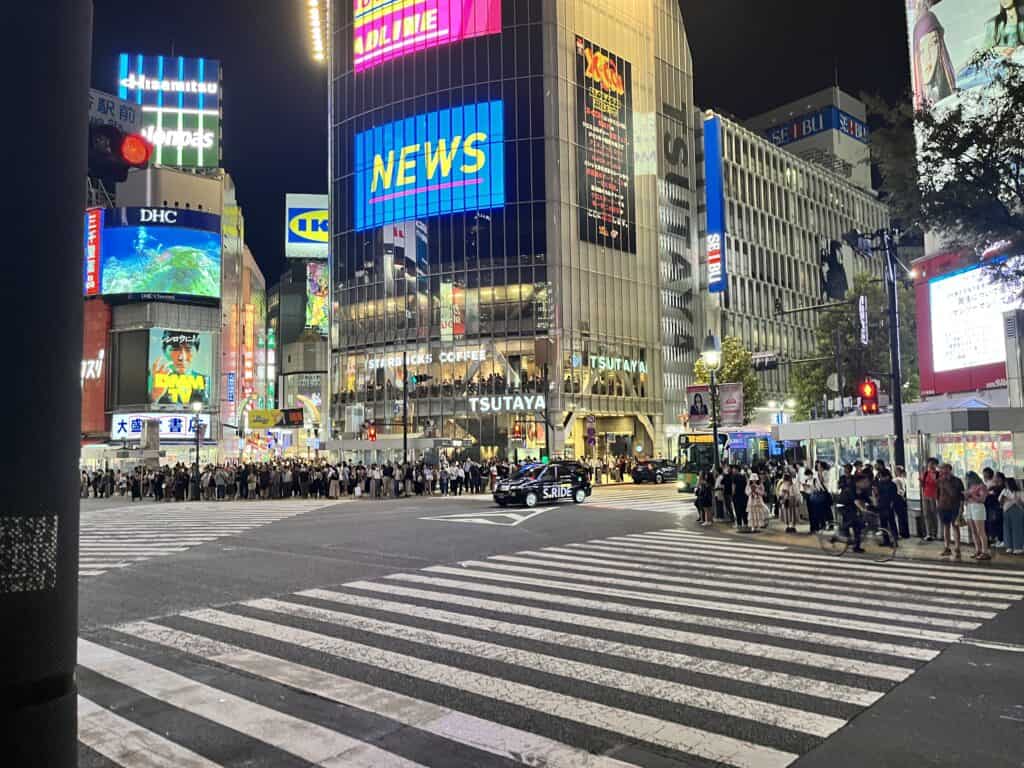 Dynamic view of Shibuya Crossing with crowds of people captured in motion, surrounded by the bustling cityscape of Tokyo, Japan