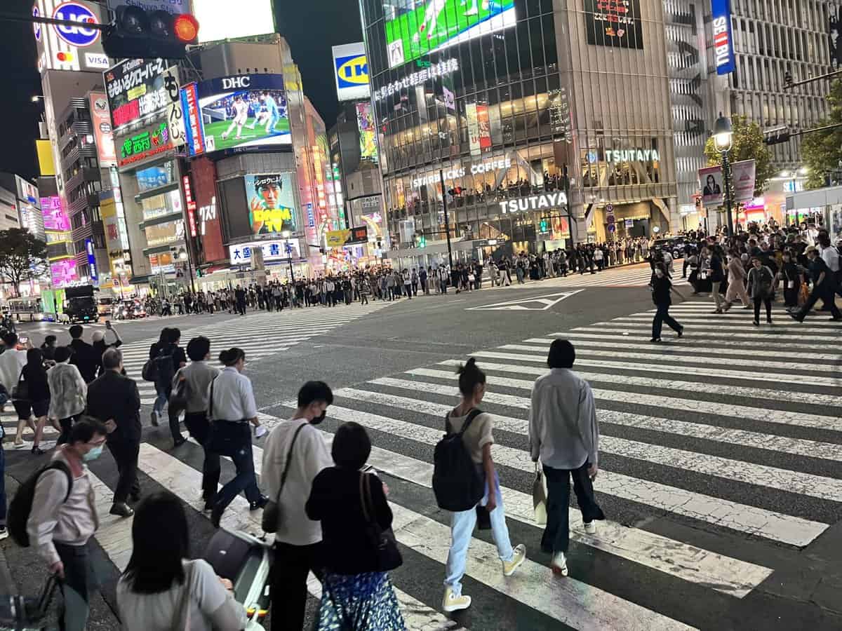 Nighttime at Shibuya Crossing illuminated by neon advertisements and a crowd of people at the heart of Tokyo's entertainment district.
