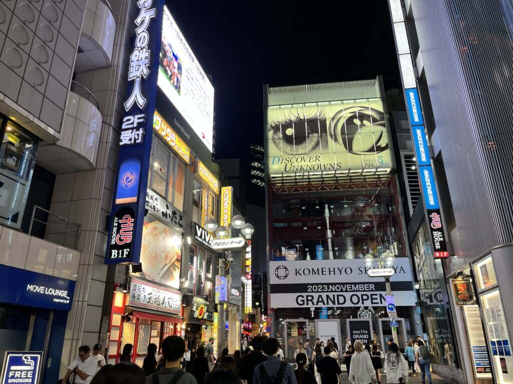 Shibuya neighborhood after dark, featuring lively crowds, street food vendors, and illuminated signs creating an energetic Tokyo night scene.
