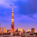 "The silhouette of Tokyo Tower stands out against the radiant hues of sunset, with the bustling city streets in the foreground