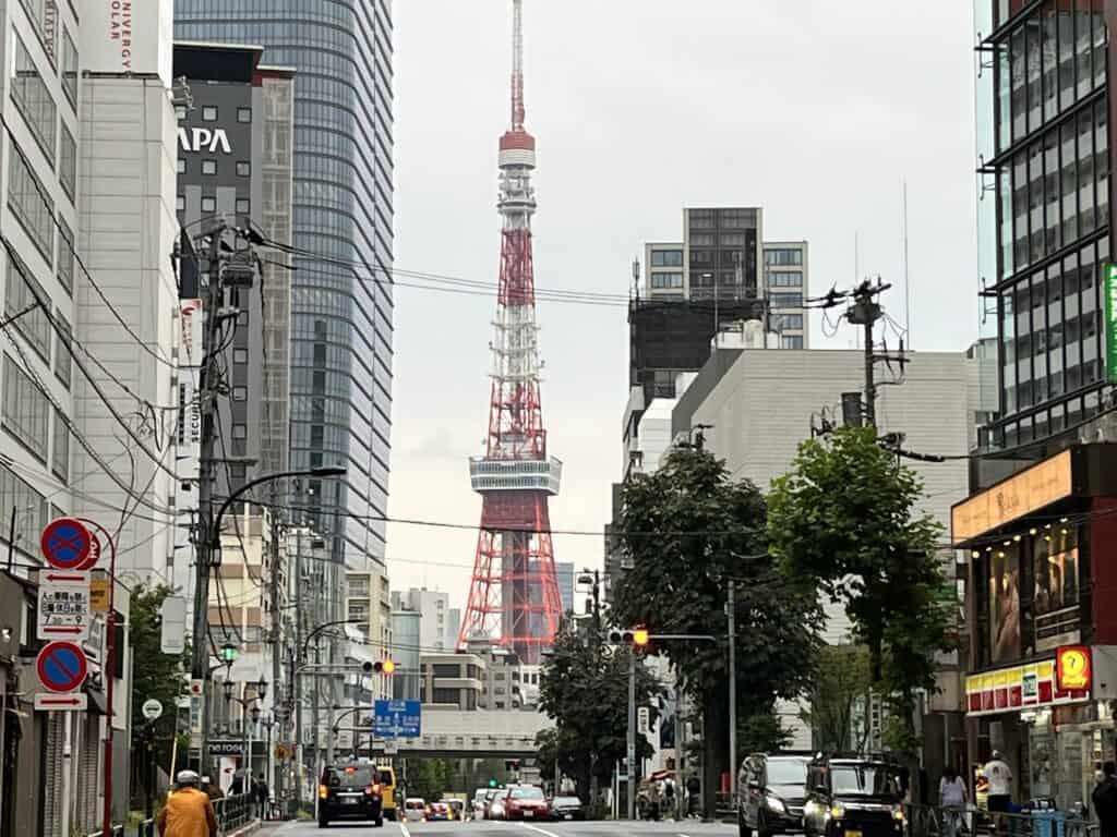 The iconic Tokyo Tower rises above the urban landscape, captured from a bustling street corner with pedestrians and traffic