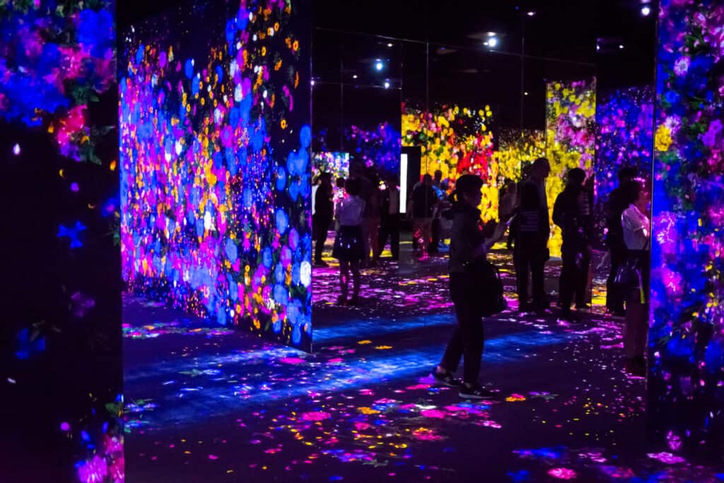 Group of visitors walking through a corridor of swirling digital flowers and butterflies in an immersive installation.