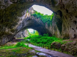 Entrance to the magnificent Devetashka Cave in Bulgaria, showcasing its vast opening and lush surroundings