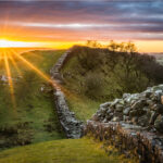 Sunset casting a golden light over the remains of Hadrian's Wall, stretching across the rolling hills of Northern England.