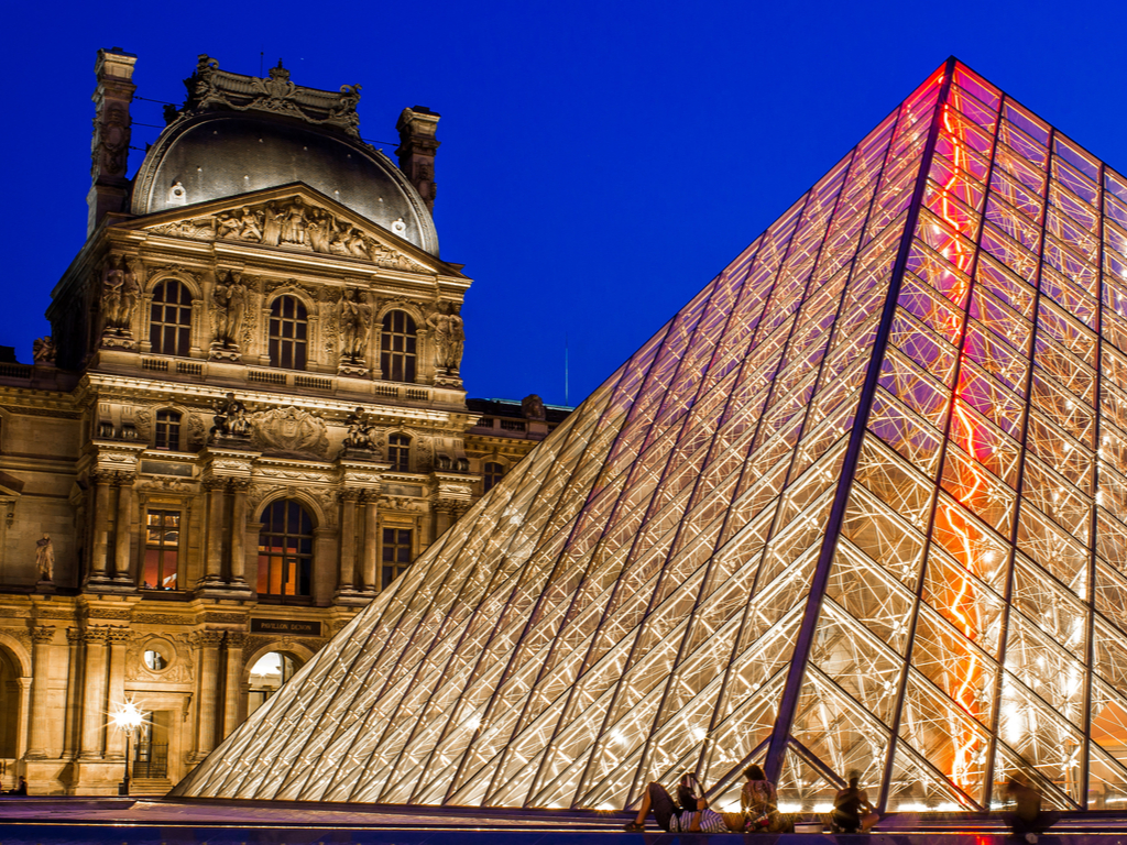 The Louvre Museum lit up at night, reflecting its grandeur in the surrounding waters
