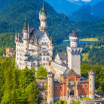 Neuschwanstein Castle perched atop a lush hill, with the Bavarian Alps in the background.