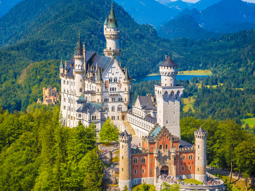Neuschwanstein Castle perched atop a lush hill, with the Bavarian Alps in the background.