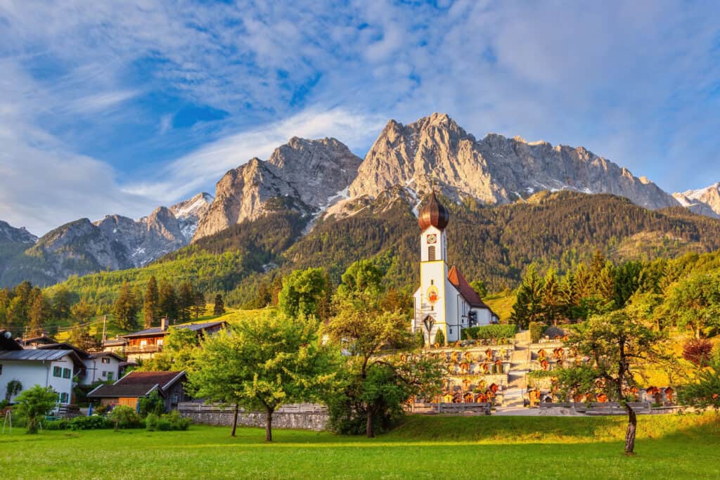 A picturesque view of Garmisch Partenkirchen in Germany, showcasing the iconic Zugspitze and the Alps with a quaint church in the village of Grainau.