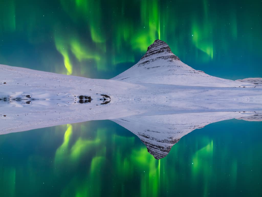 "Reflection of the Aurora Borealis in a still water body near Kirkjufell, creating a symmetrical visual.