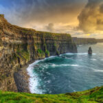 Sunset over the Cliffs of Moher, casting a golden glow on the rugged coastline.