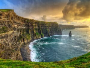 Sunset over the Cliffs of Moher, casting a golden glow on the rugged coastline.