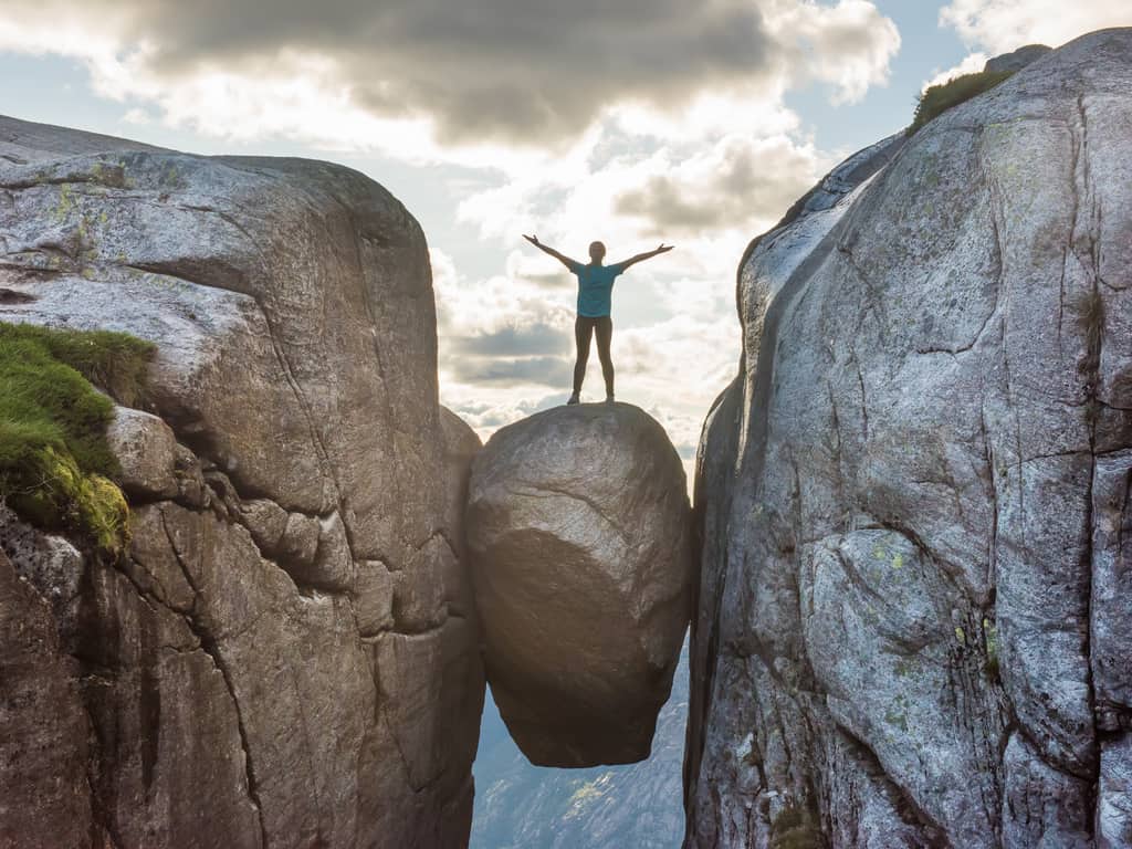 Adventurous hiker standing on Kjeragbolten, the suspended rock between two cliffs in Norway, with a breathtaking view